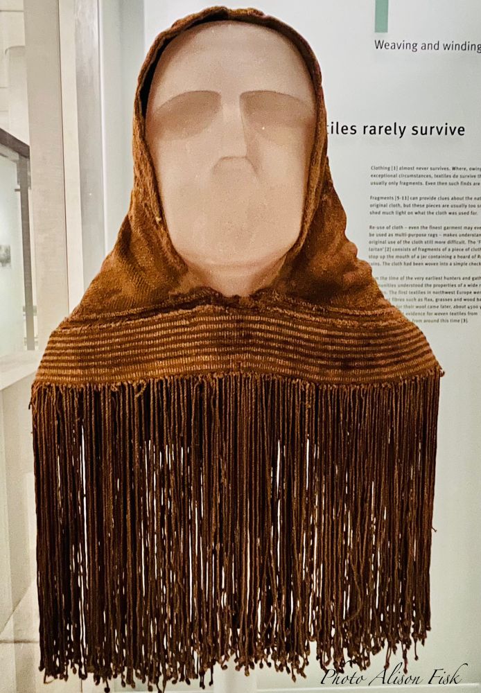 My photo shows a mannequin wearing a brown-coloured woollen hood with long knotted fringe on display at the National Museum of Scotland in Edinburgh. It was found in peat moss on the island of Orkney in 1867. Organic clothing rarely survives. This woven hood is remarkably well-preserved for its age. Radio-carbon dated to AD 250 - AD 615.