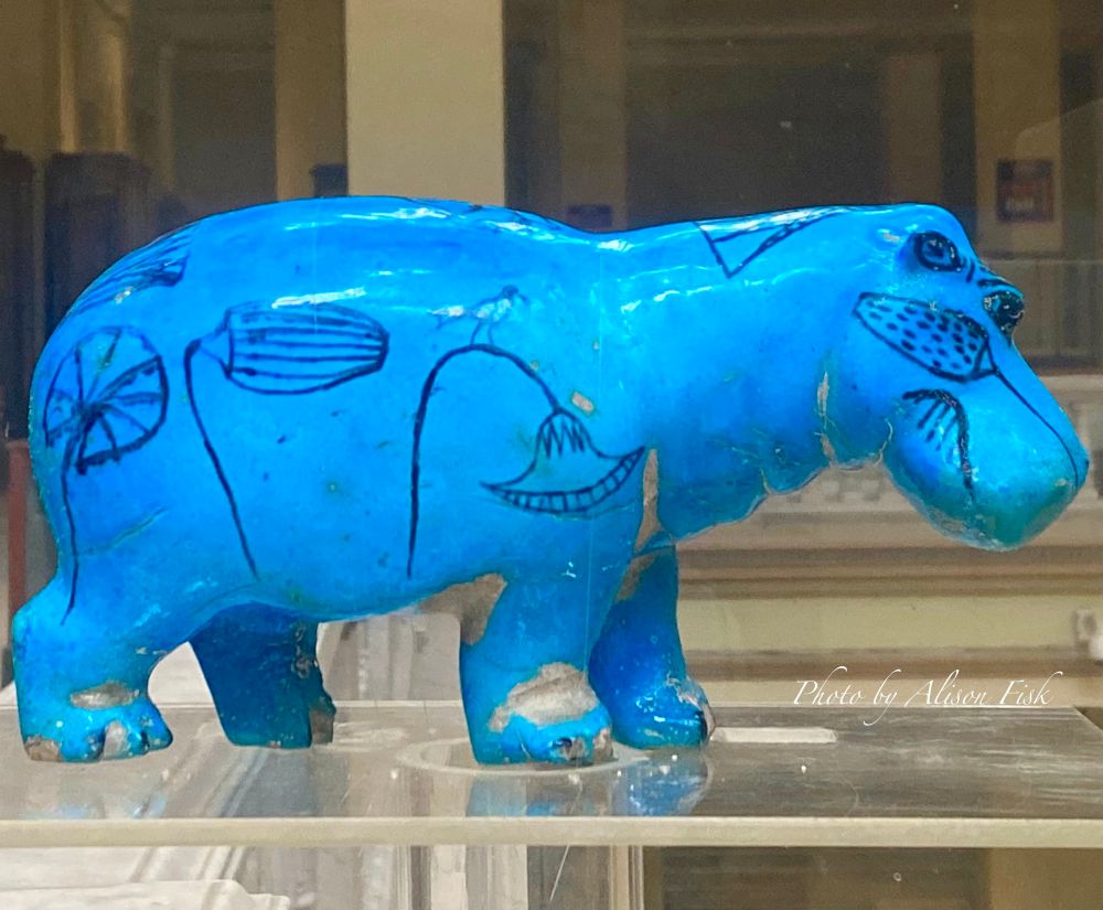 My photo shows an ancient Egyptian statuette of a standing blue hippopotamus  on display at the Egyptian Museum in Cairo. It is made of Egyptian faience, a ceramic material coated with a bright blue glossy glaze. The hippo is viewed from the side profile with head on the right. It is decorated in black pigment with outlines of lotus plants which grow in the hippos Nile habitat. A little bird is perched on the stem of one lotus flower. Dimensions: Height 11.5 cm, length 21.5 cm.

Excavated by Auguste Mariette in 1860 at the necropolis of Dra’ Abu el-Naga’, western Thebes. Dated Middle Kingdom, 11th Dynasty, c. 2134-1991 BC.

Egyptian faience is a ceramic material made of quartz. Blue hippos are decorated with black pigment outlining depictions of Nile river plants, in particular lotus flowers. In ancient Egypt lotus flowers had religious symbolism; the flowers close at night and reopen with the rising of the sun in the morning, which was associated with regeneration and rebirth. 

Blue faience hippos have been found in Middle Kingdom and Second Intermediate period tombs. It’s thought they were placed there to help the rebirth of the deceased. Associated with the life-giving Nile, regeneration, and Tawaret, the ancient Egyptian goddess of fertility and childbirth.

Hippos were also seen as dangerous to humans so the legs of faience hippos have often been broken off the statuettes found in tombs, perhaps to make sure the hippo could not harm the deceased in the afterlife.