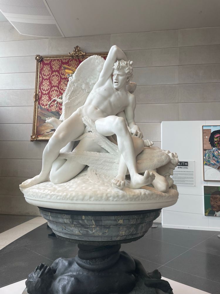 A marble sculpture depicting fallen angels in a classical style. The male angels are shown with expressions of ecstasy. 