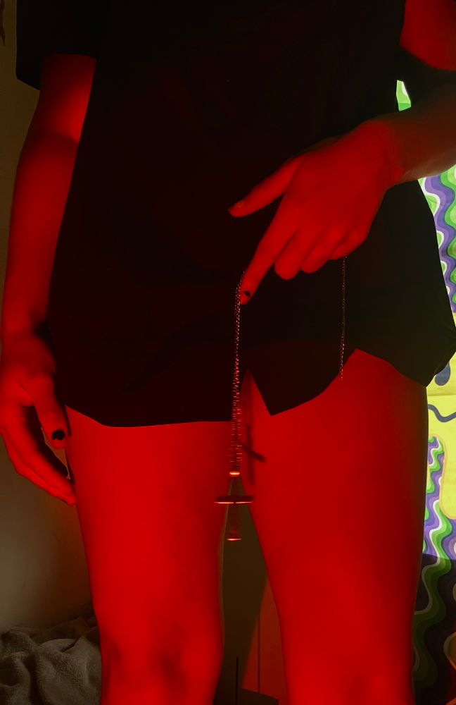 Image of me standing, holding a cross necklace between my legs and wearing a priest shirt. You can see bright red lights reflecting off my skin