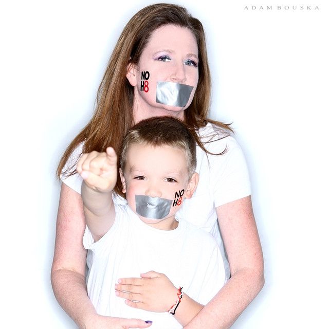 1 woman and 1 kid, NOH8 temporary tattoo on their cheeks, duct tape on their mouths symbolizing the attempt to silence the LGBTQ+ community. 