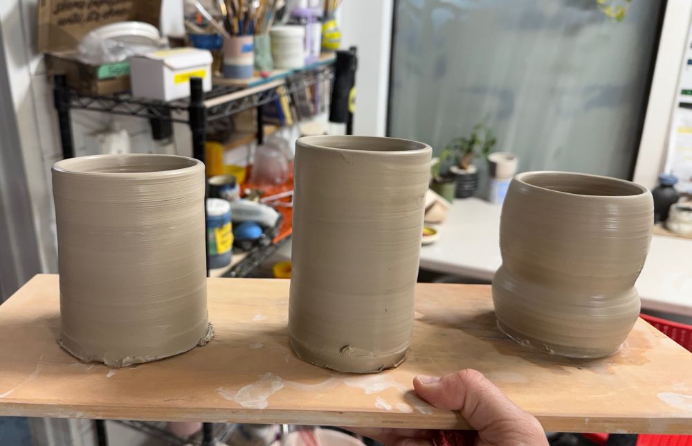 Three freshly thrown clay cylinders on a wood board. 