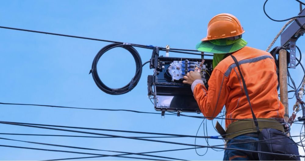 A lineman suspended in air works inside fiber splice case amid utility lines 