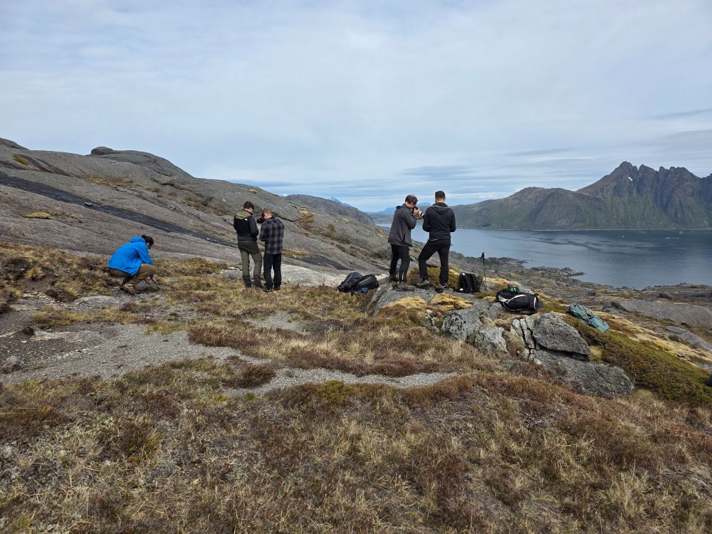 Two reseachers taking notes while being filmed by two camera men in the scenic background of the Lofoten islands.