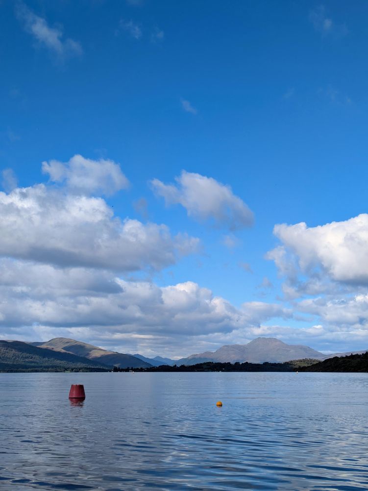 View up Loch Lomond with colourful buoys on the loch in the foreground and mountains in the distance 
