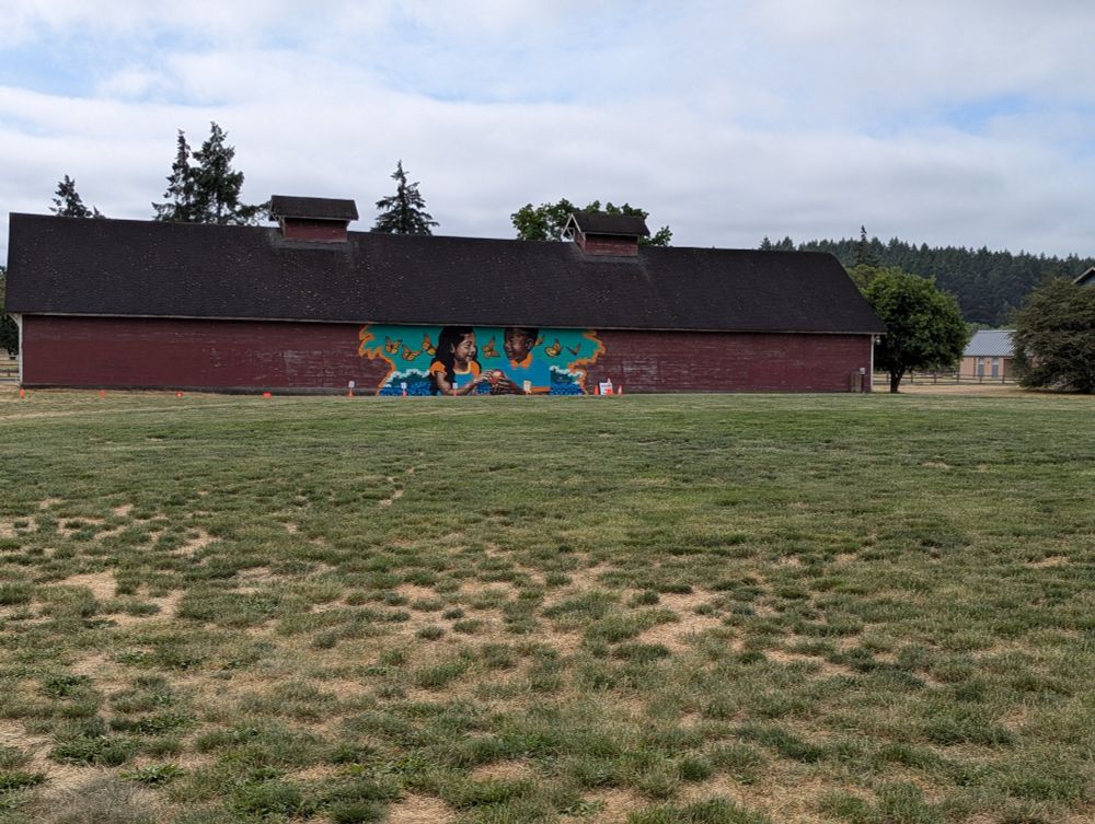 A photo of a big red barn with a rainbow mural of an Asian girl and Black boy with a bunch of butterflies 