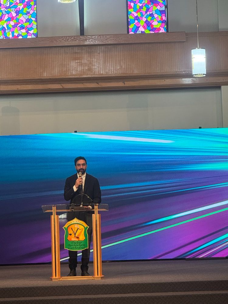 Zohran at the pulpit, holding a mic.