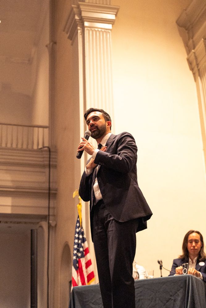 Zohran on stage holding a mic and addressing the forum.