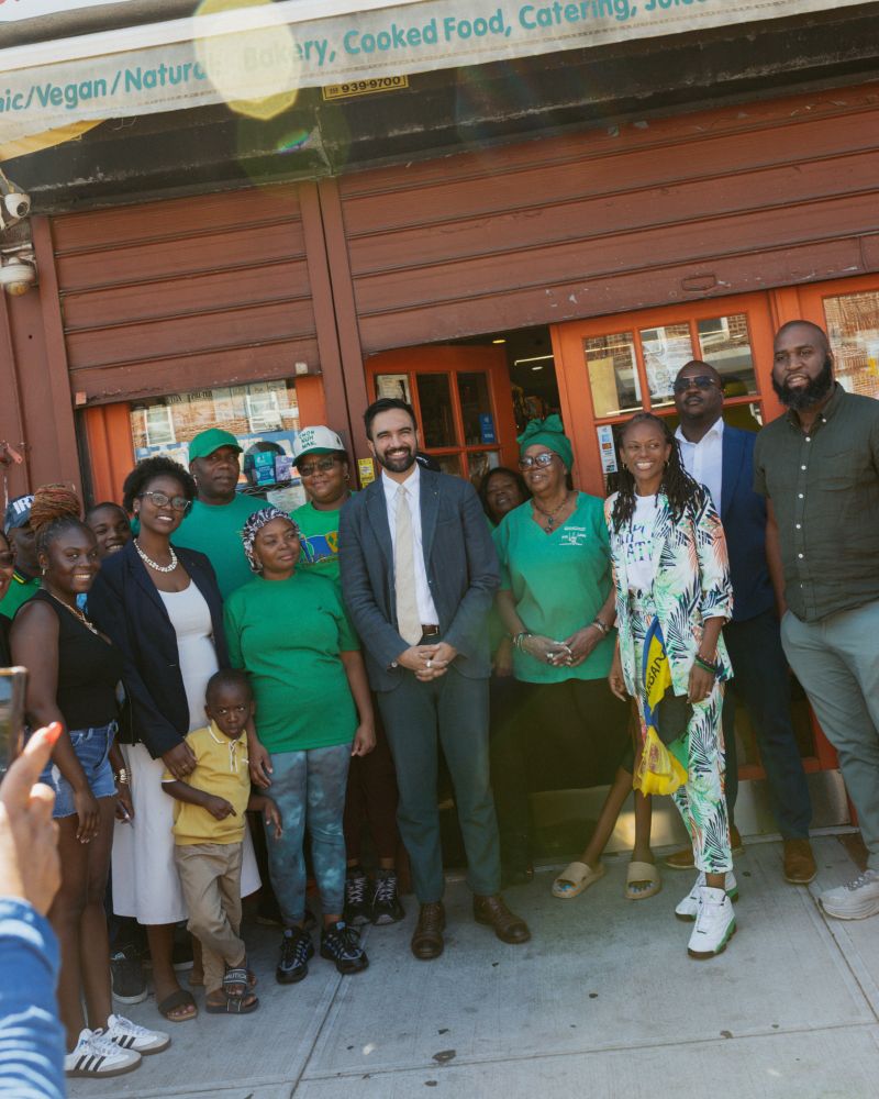 A group photo of Zohran and the walking tour in front of a small business. 