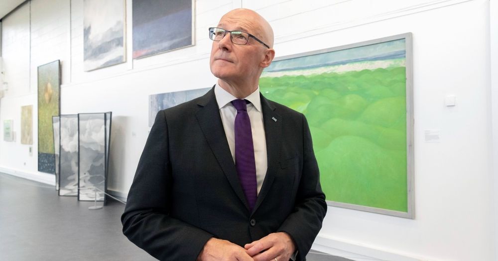 First minister John Swinney looks to the side in front of paintings from the exhibition 