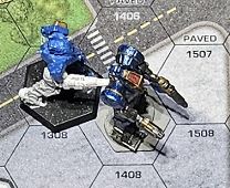 An image of a Classic BattleTech game in progress, using one of the City BattleMats as the ground.
A Wolfhound BattleMech is bullying a Zeus BattleMech (which weighs over twice as much) by continually pouring laser fire into its rear armor. Already some of its weapons are off-line, and now it is in danger of more serious internal component damage.

... not trying to evade the Wolfhound was a mistake.