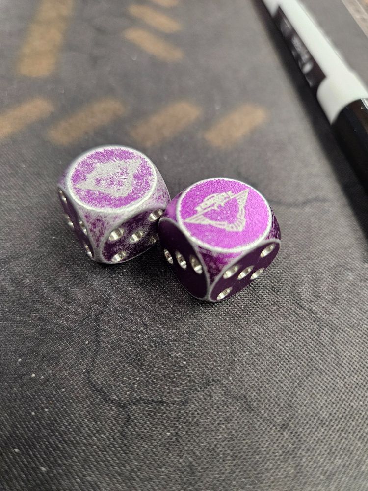 A photo of two six sided metal dice, with most of the color rubbed off one. 