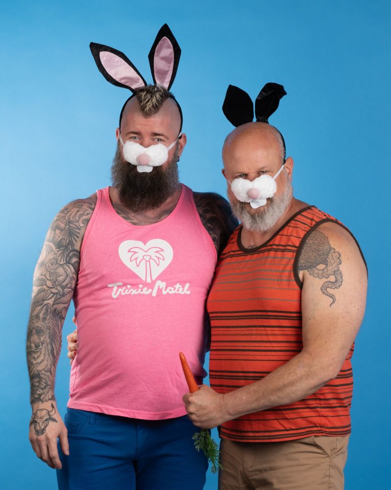 Eric and Mike posing together, both wearing bunny ears and a bunny nose in front of a blue backdrop . Eric is  holding a plastic carrot. 
