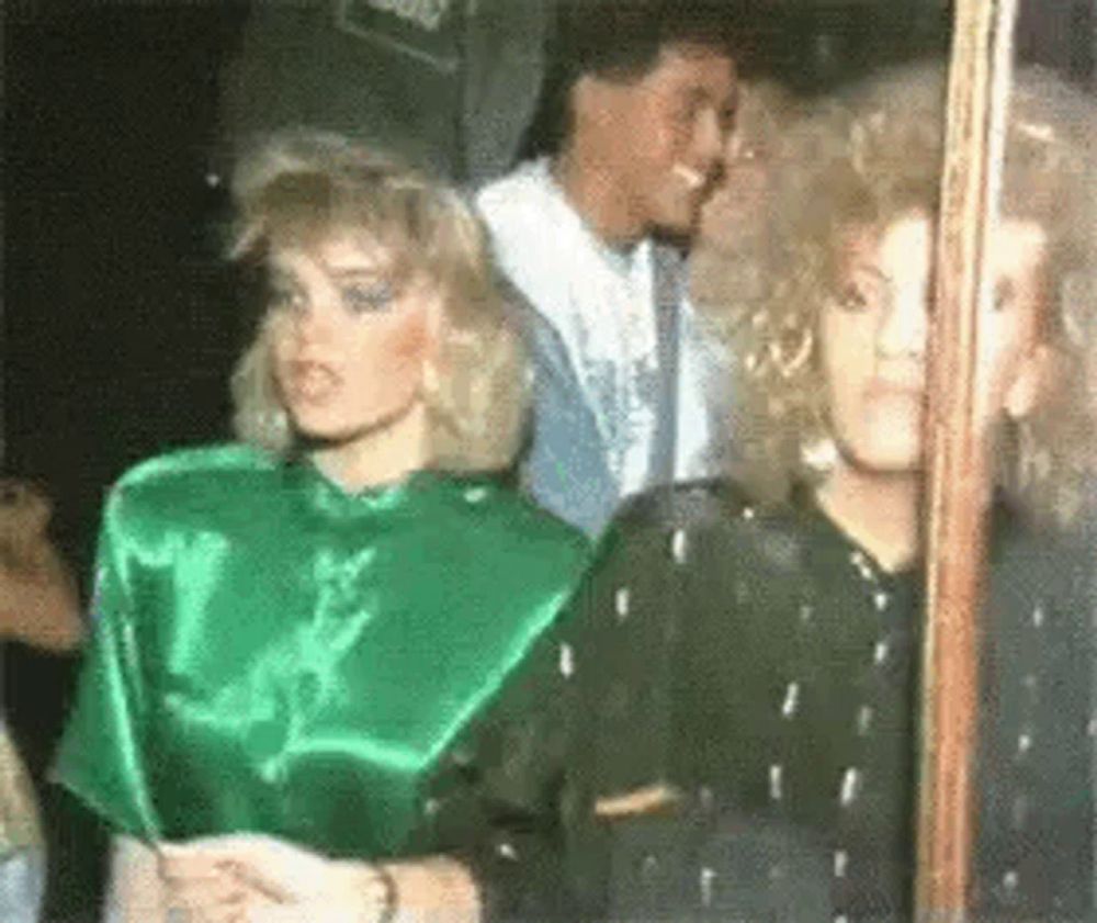 a group of women are standing next to each other in a room . one of the women is wearing a green satin top .