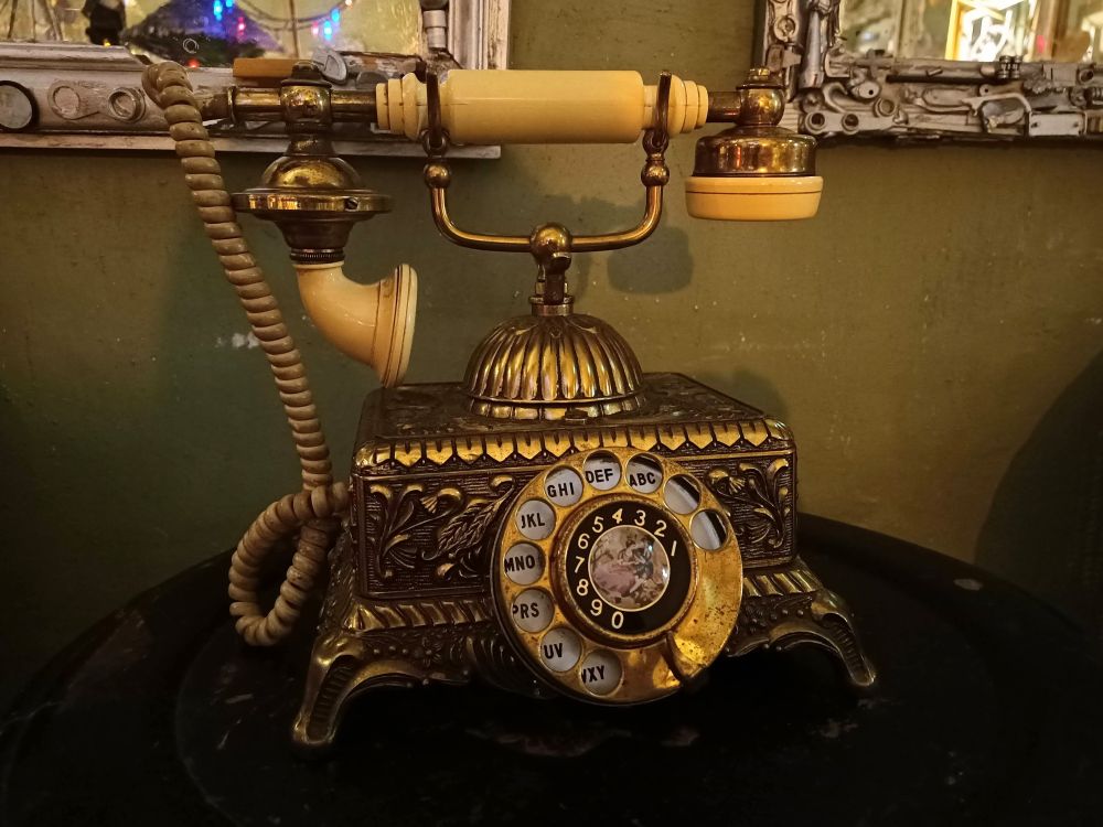 Kleine runde dunkle Tischplatte,ein goldenes, verschnörkeltes Telefon,steht darauf, Wählscheibentelefon 