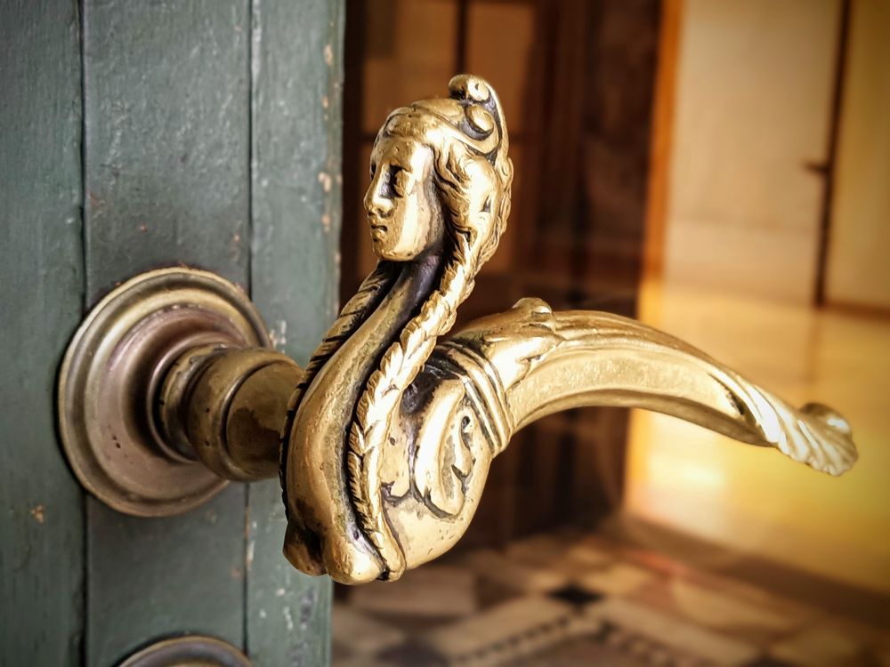 Goldener,leicht verschnörkelter Türgriff mit Frauenkopfform 
