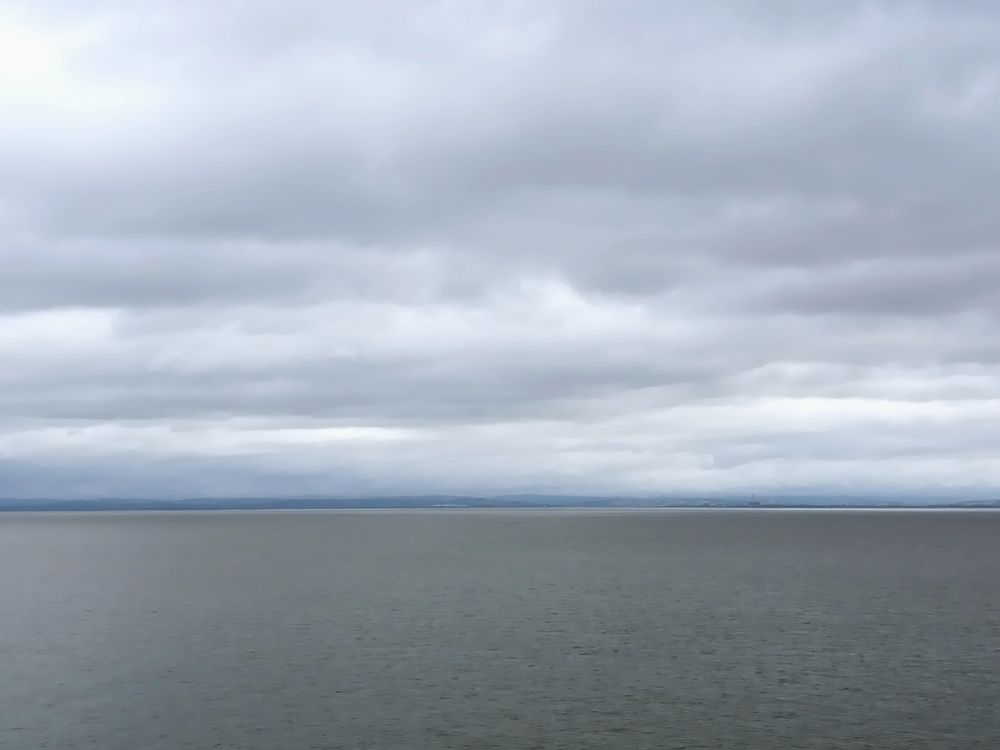 Wasserfläche grau, minimaler Horizont leicht bläulich,grauer Wolkenhimmel 