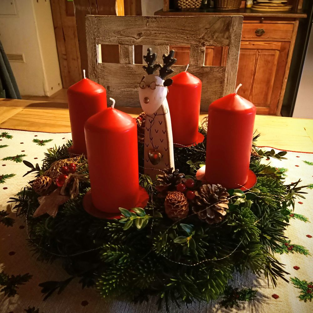 Adventkranz mit 4 dicken roten Kerzen, Zapfen und Goldfäden, steht auf einem weihnachtlichen Tischläufer auf einem Holztisch 