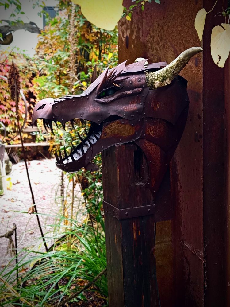 Metallener Drachenkopf als Schmuckelement an einer rostigen Metallplatte befestigt,etwas grün im Hintergrund 