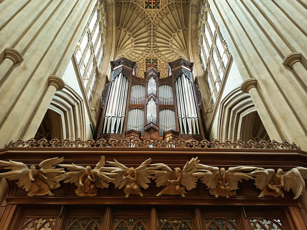 Oberes Ende einer mehrflügeligen Holztür,6 Engelsfiguren mit unterschiedlichen Instrumenten,dahinter Orgel und rechts und links hohe Sandsteinsäulen des Seitenschiffs der Abbey