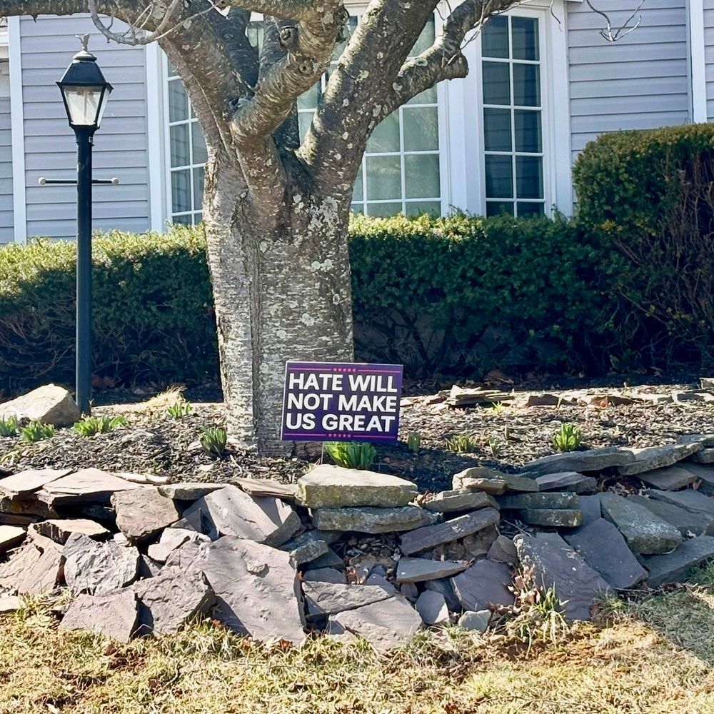 A yard sign that says “Hate will not make us great” under a tree in front of a house