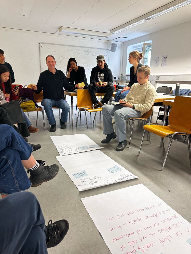 A group of people sitting in chairs holding a discussion around big pieces of paper on the floor