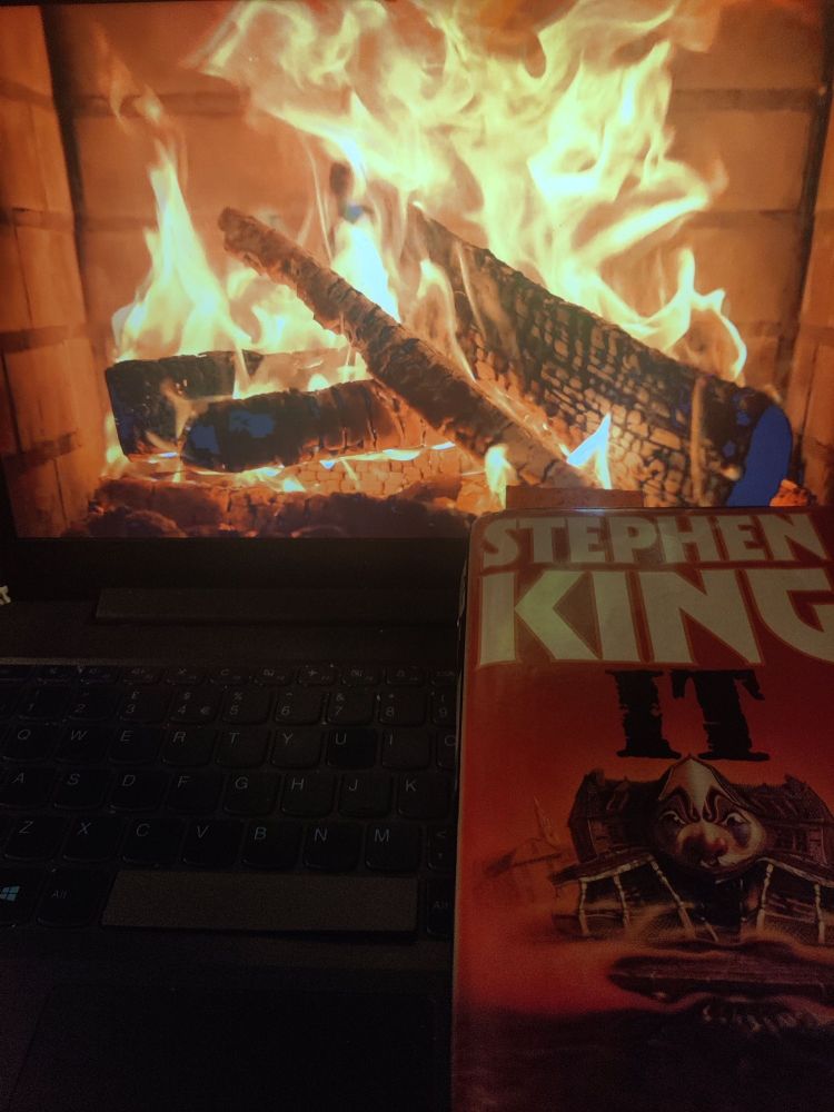 Laptop with a video of a fireplace and the book "IT" by Stephen King on top.