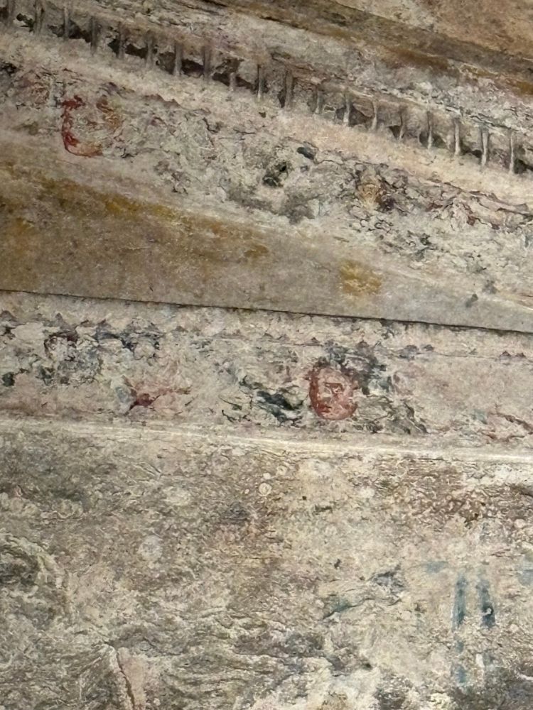 Faded details along the pediment of the upper level of a hypogeum, sporting masks