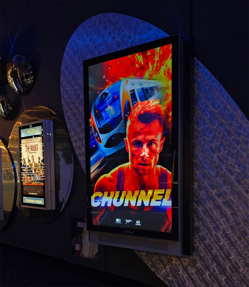 A video screen displaying a poster for a fake movie called Chunnel, with some supposed action star looking sweaty in the foreground while a train races away from an explosion behind him.