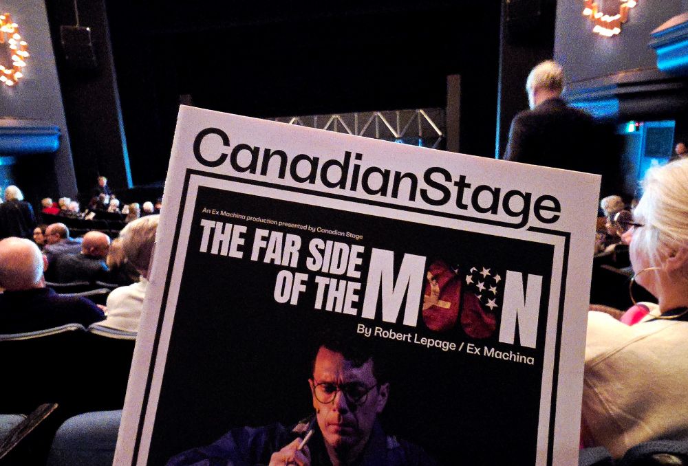 A view from a seat at the Bluma Appel theatre, with a Canadian Stage playbill for The Far Side of the Moon held up in front.