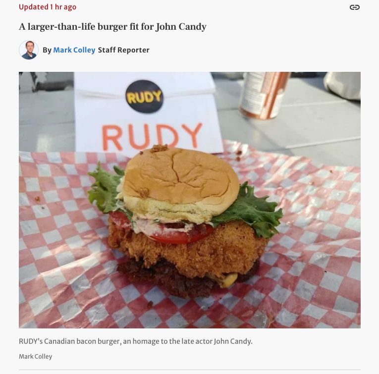 A screencap from the Star's TIFF live blog. This entry carries the headline "A larger-than-life burger fit for John Candy"

There's a photo of a kind of monstrous burger with a giant deep-fried slab on it. The caption reads: "RUDY’s Canadian bacon burger, an homage to the late actor John Candy."
