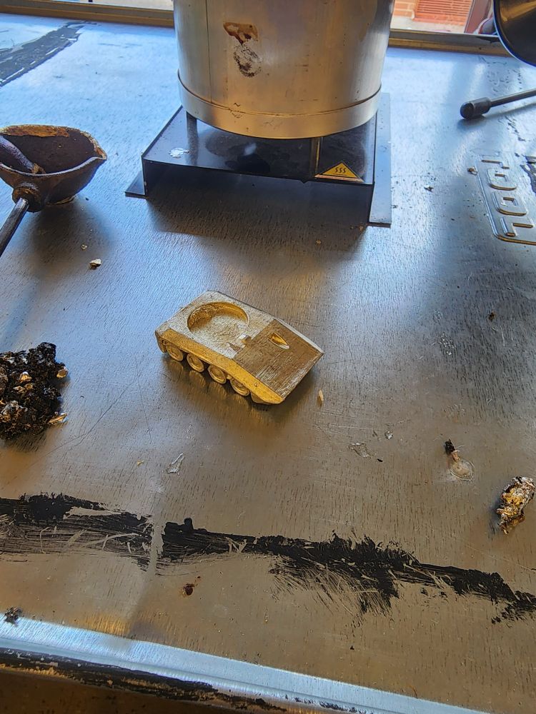 A small silvery metal tank in front of a casting pot