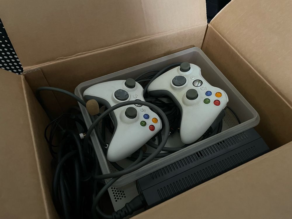 Cardboard box with cables and components inside, with two white Xbox 360 controllers showing face up.