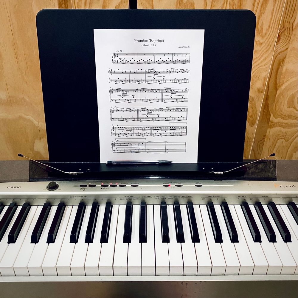 A square photo of a Casio keyboard in front of a wooden wall with some sheet music for a beginner-friendly arrangement of Promise (Reprise) by Akira Yamaoka from the Silent Hill 2 OST