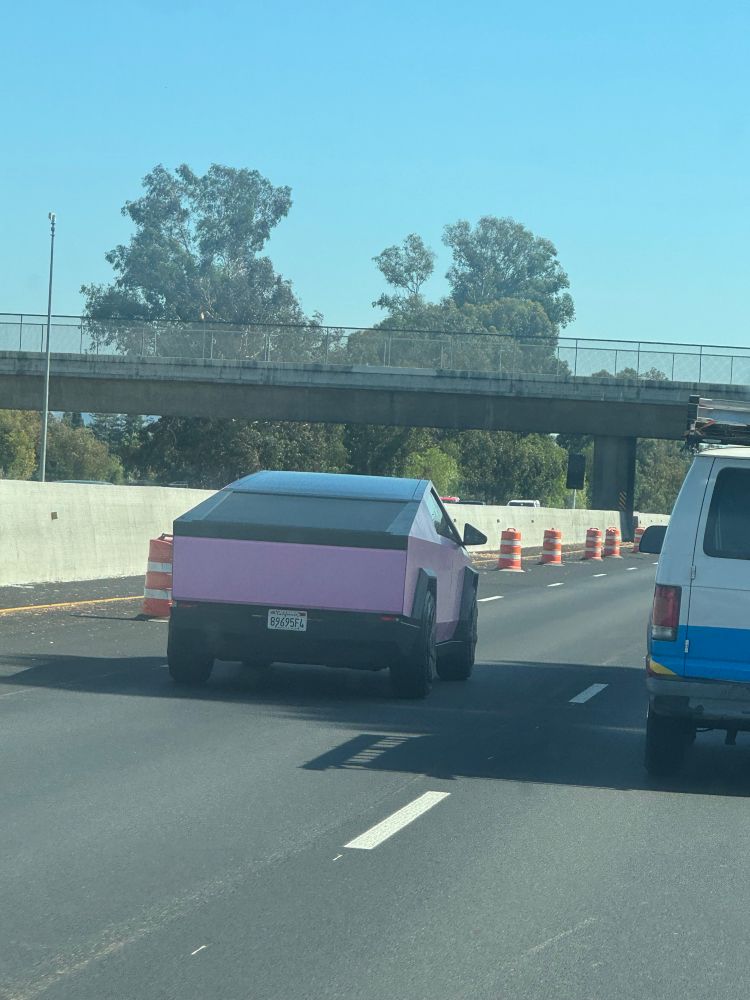 A pink cyber truck driving on a highway, driven by a fascist