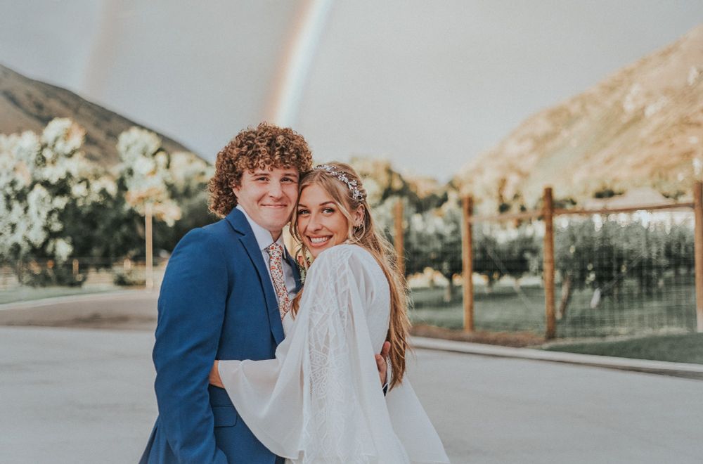 couple smiles broadly in front of a rainbow