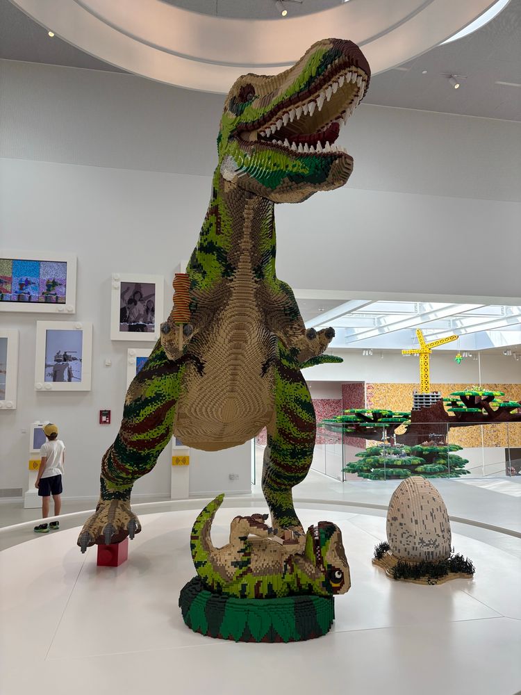 Lego dinosaurus in het legohouse met op de achtergrond de Lego tree, een boom volledig van legoblokjes in het trappenhuis 
