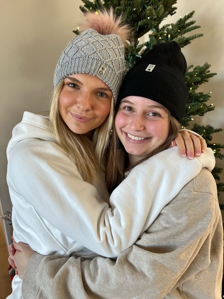 Two women wearing beige and gray sweatsuits and Sioux Falls City FC winter hats.