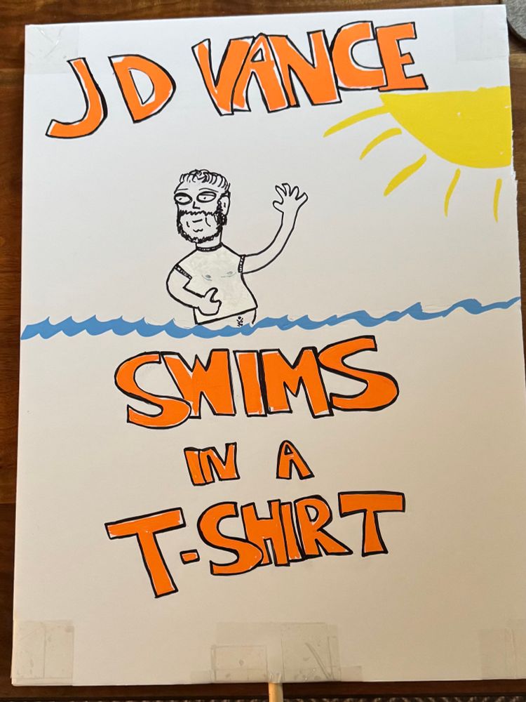 Protest sign of poorly drawn JD Vance swimming in a t-shirt. His nips can be seen thru the wet t-shirt material. The slogan reads: JD Vance swims in a t-shirt. 