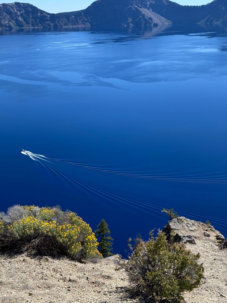 Boat sending out ripples on a completely calm and deep blue Crater Lake. 