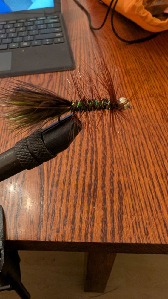 Olive, black, brown fly in a fly tying vice. 