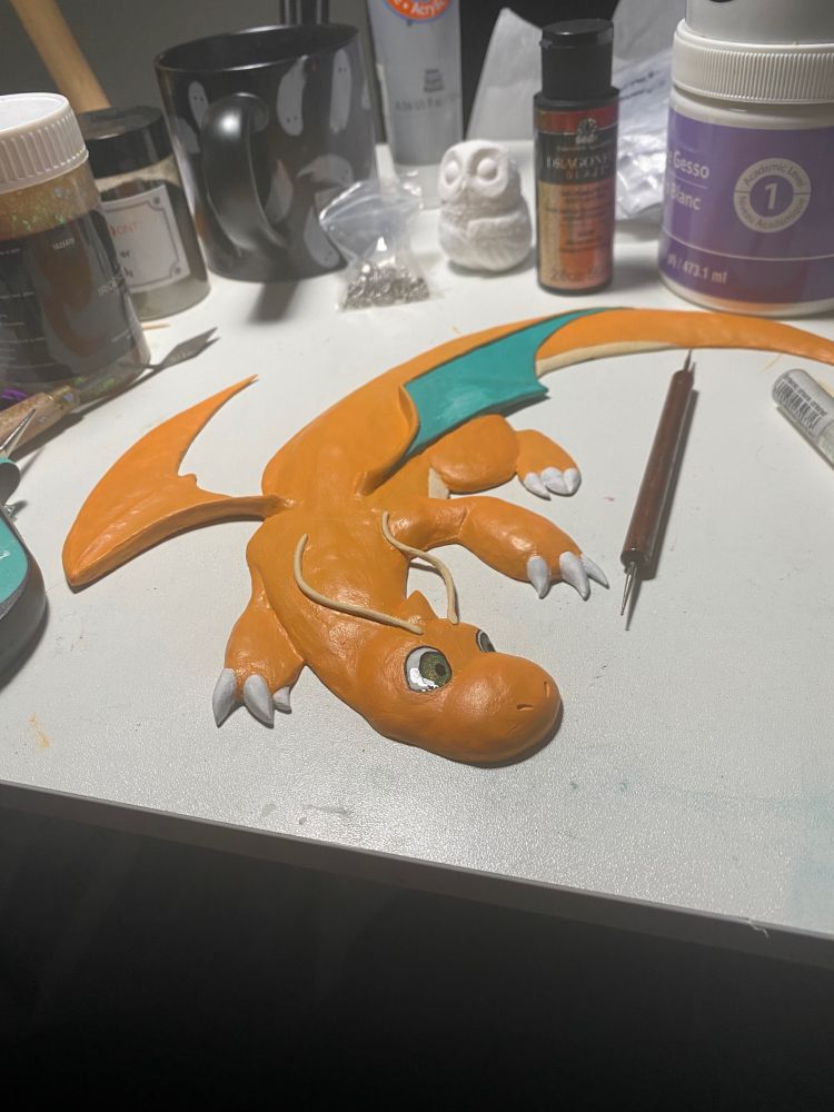 A relief of Dragonite made from clay sits on a cluttered desk. The Dragonite swoops with its neck craned to the right.
