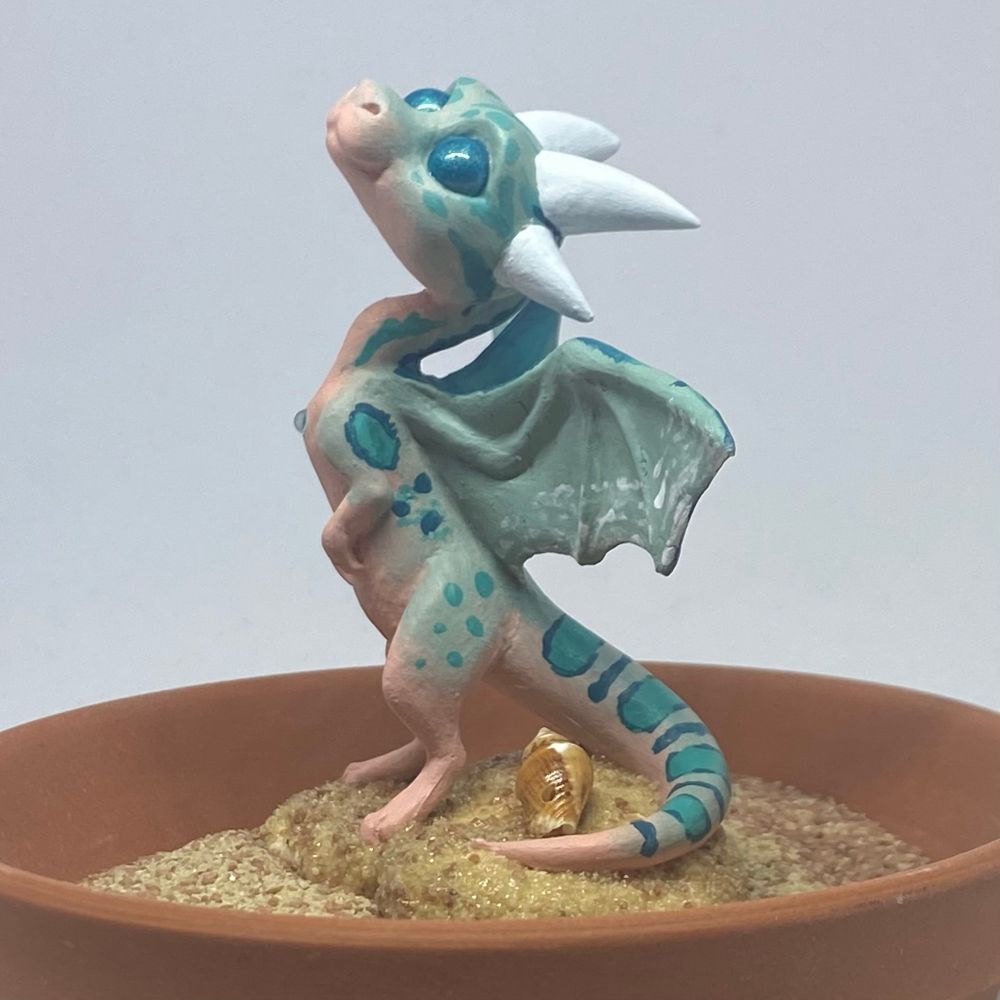 A sculpture cast of a little dragon, painted beachy colors. It stands on its hind legs with its wings spread.