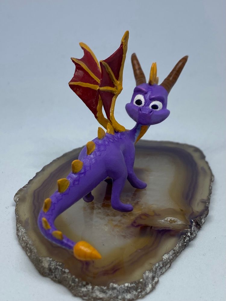 A polymer clay sculpture of Spyro the dragon, looking back over his shoulder inquisitively.
