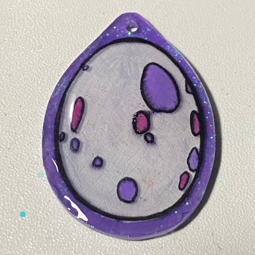 A handmade keychain of a dragon egg with purple and pink patches