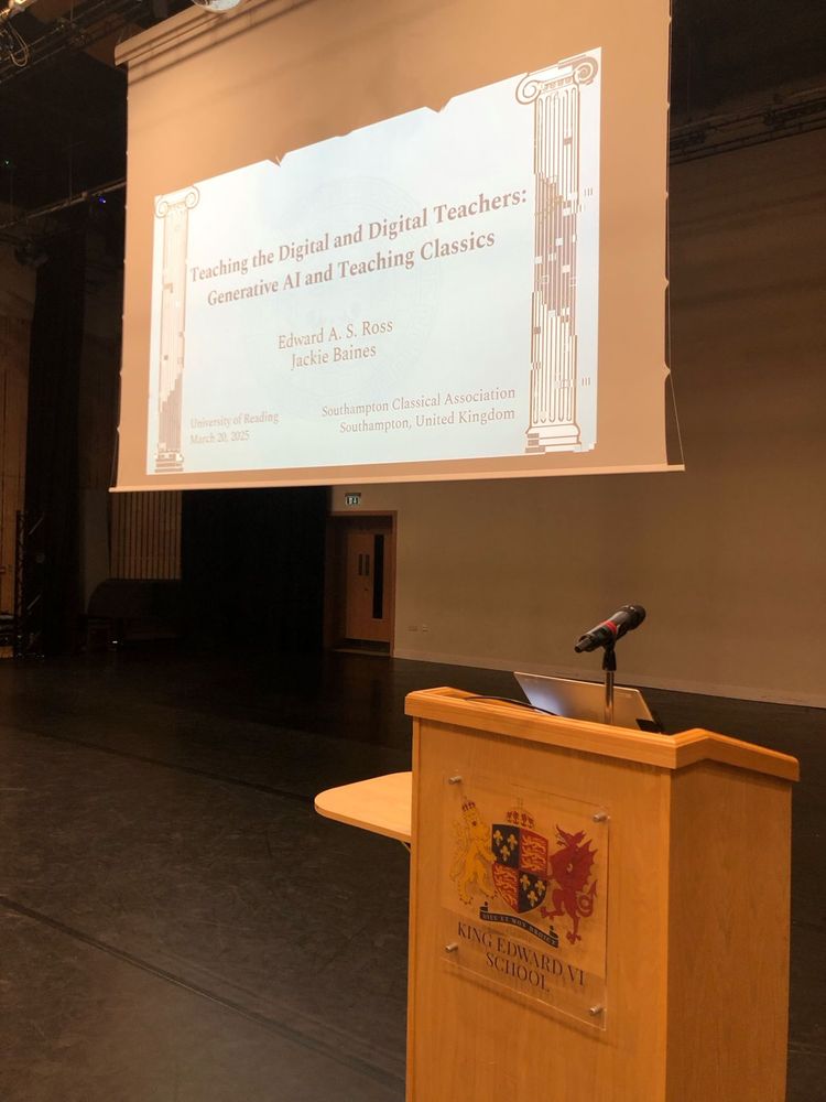 An image of a theatre stage. In front, there is a wooden podium with a crest for King Edward VI School. In the back is a projector screen displaying a slide that reads “Teaching the Digital and Digital Teachers: Generative AI and Teaching Classics”