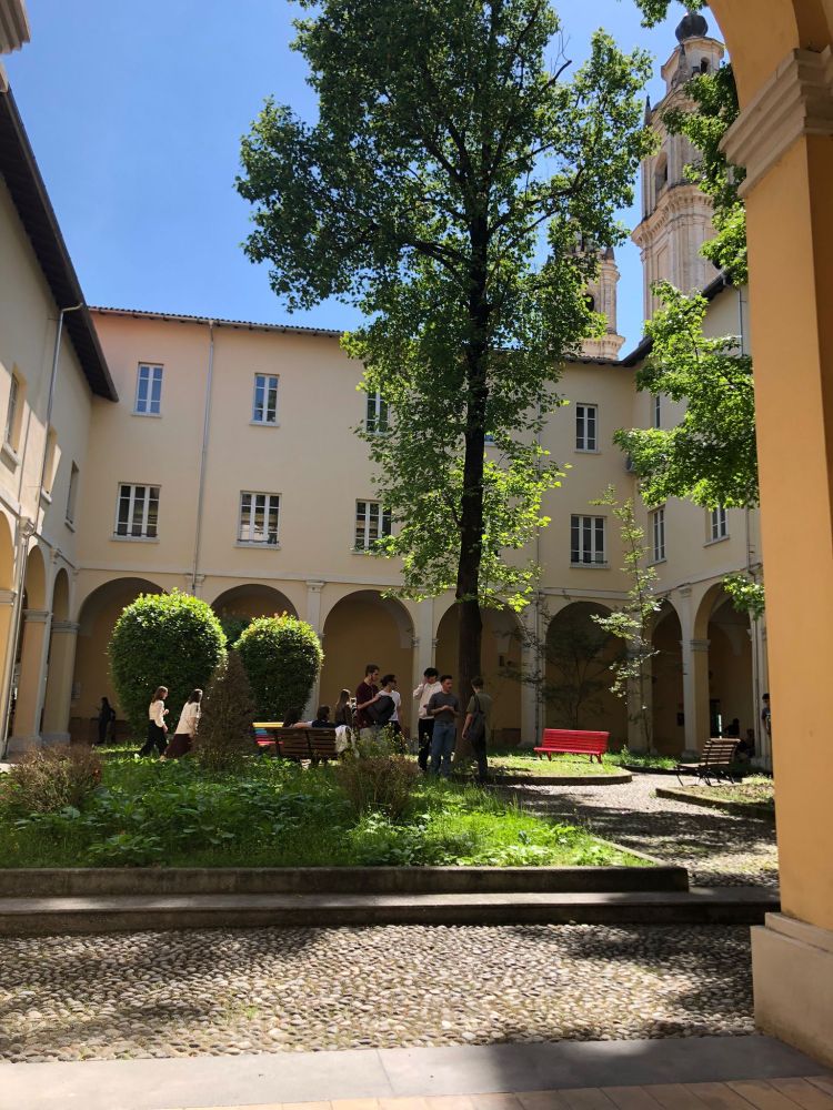An open air garden in the middle of a yellow building with arched porticos. There is a large tree in the middle.