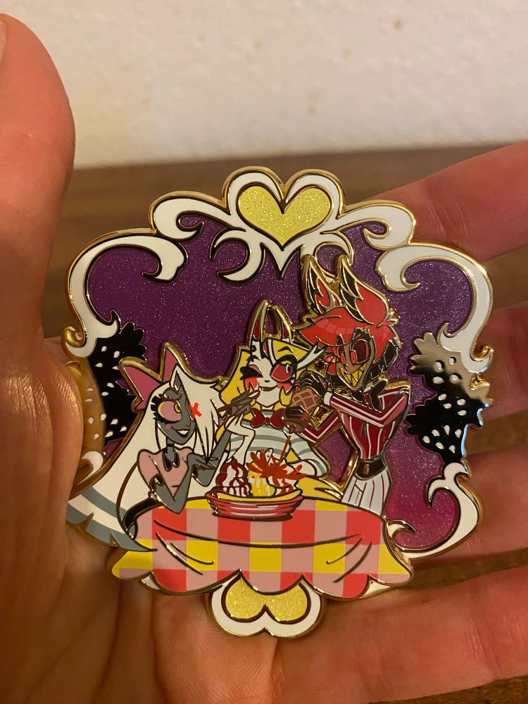 An enamel pin of Charlie Morningstar, Vaggie, and Alastor from Hazbin Hotel on an ice cream date.