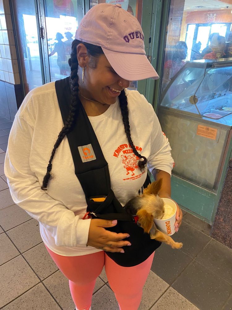 Zeph holding Chloe in a sling while she licks a pup cup treat