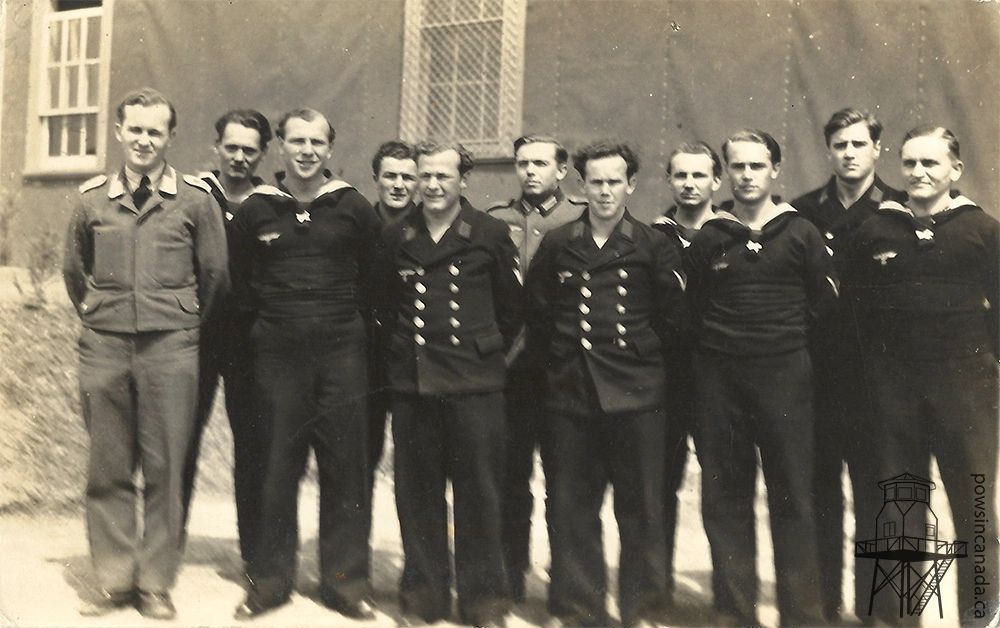 Black and white photo of German soldiers, sailors, and airmen standing in front of a building. They are prisoners of war at Camp 23 (Monteith).